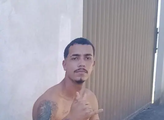 Imagem de um jovem fazendo um sinal com a mão, durante uma foto.