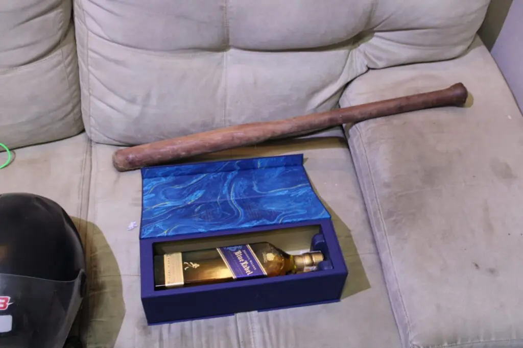 Imagem de um sofá com uma caixa de whisky Blue Label e um taco de beisebol.