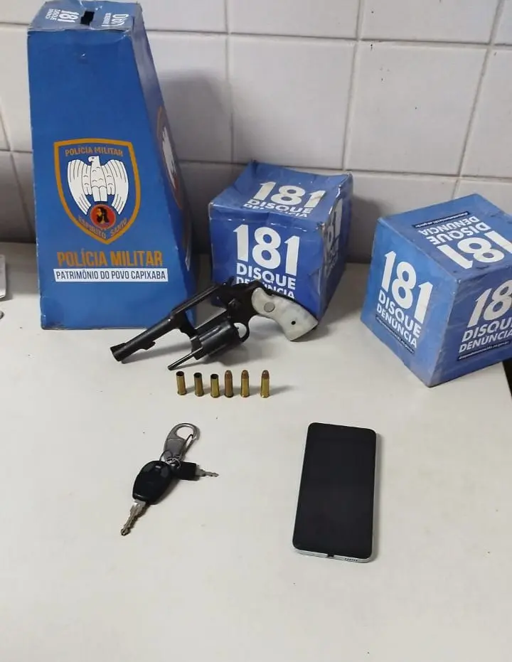 Sobre uma mesa um revólver calibre .38 3 munições e 3 capsulas deflagradas, um celular e uma chave. 