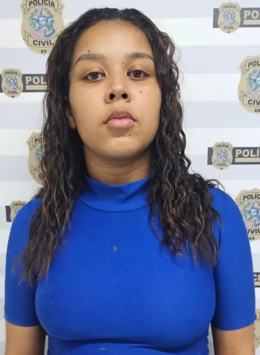 Imagem de uma mulher (Agatha Joyce da Silva Nascimento, de 20 anos) em frente a uma parede com imagens de divulgação da Polícia Civil.