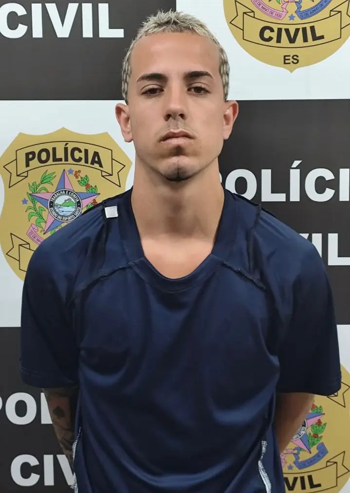 Imagem de um homem (Everton Júnior Pena Nunes, vulgo “Goe”, 20 anos) em frente a uma parede com imagens de divulgação da Polícia Civil.