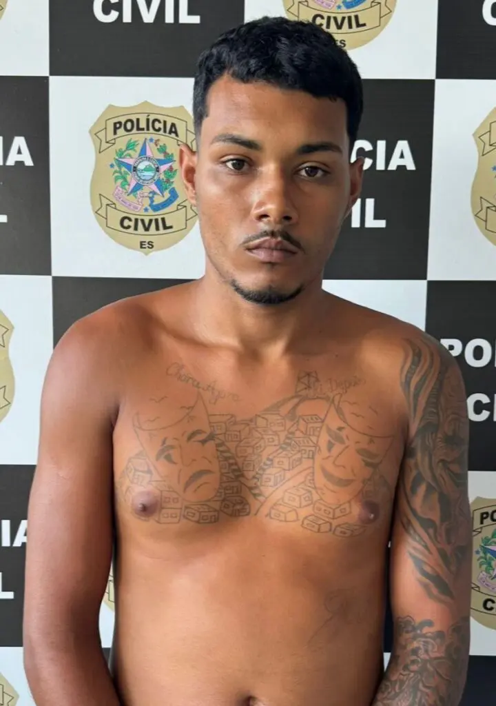 Imagem de um homem (João Gabriel Costa Vieira, vulgo “GB”, 25 anos) em frente a uma parede com imagens de divulgação da Polícia Civil.