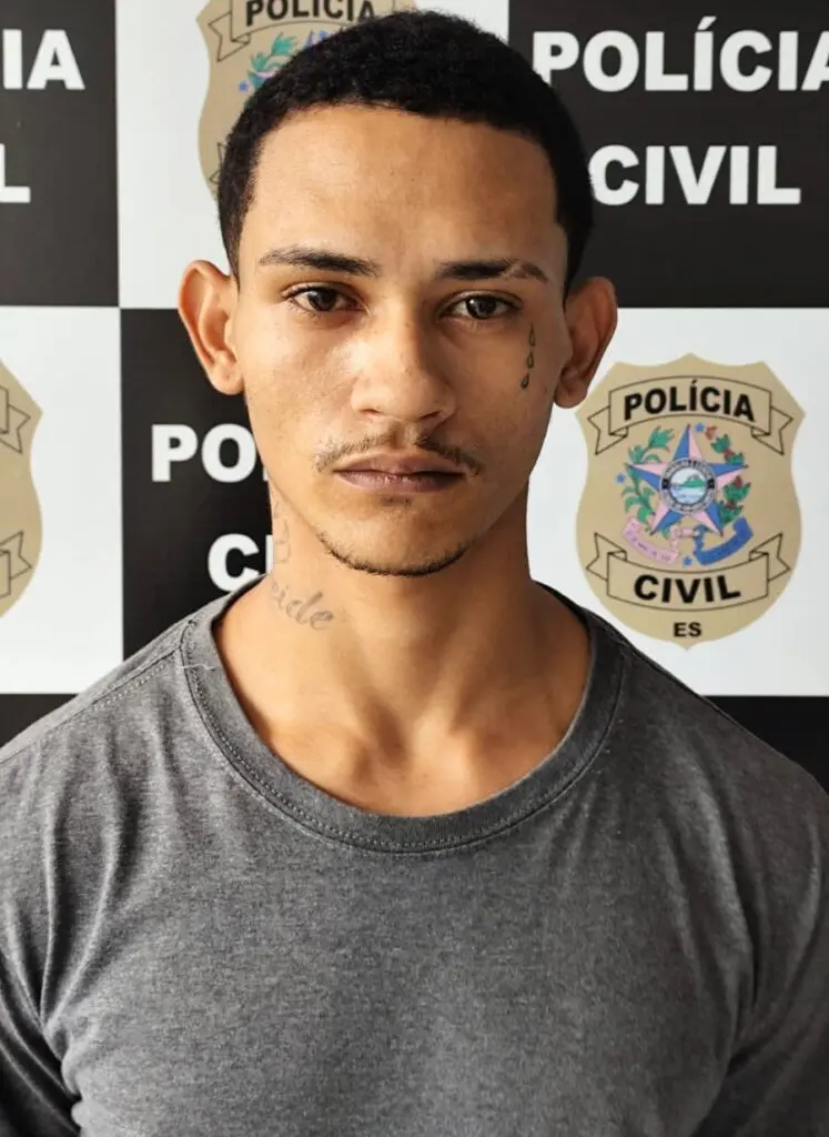 Imagem de um homem (Daniel Bredoff Firmino, vulgo “Ceará”, 27 anos) em frente a uma parede com imagens de divulgação da Polícia Civil.