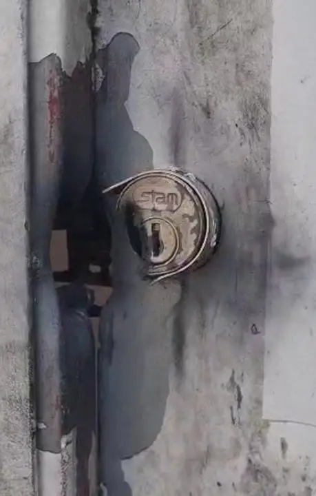 Imagem da fechadura de um portão  danificada, com uma marca de tiro.