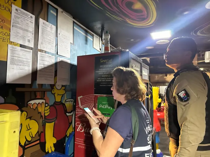 Imagem de uma fiscal ao lado de um policial durante uma vistoria em um bar.