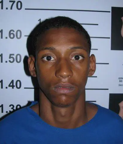 Imagem de um homem (Valter Santana Costa, de 21 anos), acusado de participar de uma quadrilha de furtos de moto, parado em frente a uma parede onde ha uma marcação de metros, usada pela polícia para realizar a fotografia e identificação de detidos.