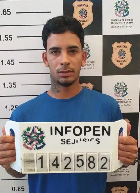 Um homem (Higor Nunes Teixeira, de 22 anos) segurando uma placa de identificação, e na parede ao fundo identificações da Polícia Civil.
