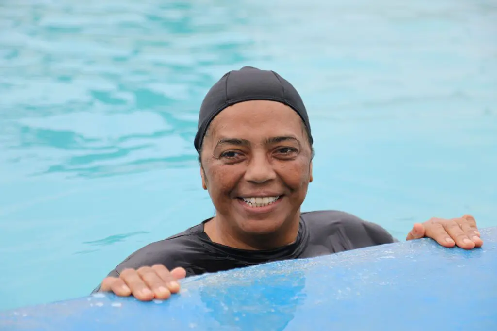 Imagem de uma idosa (Adriana Rainha, de 57 anos) segurando na borda de uma piscina.