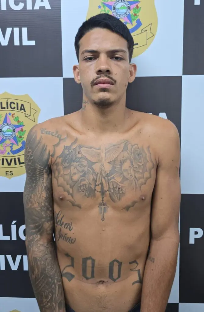 Imagem de um homem (Ryan Inácio Silva, de 22 anos) em pé em frente a uma parede com as identificações da Polícia Civil do ES.