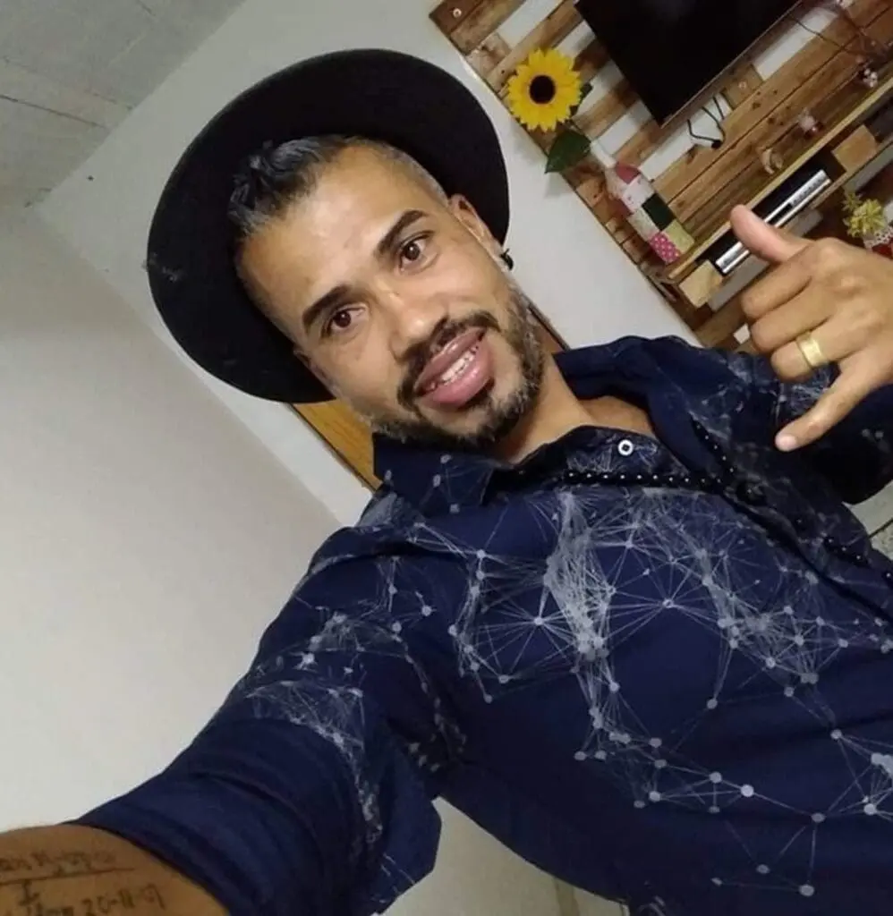 Imagem de um homem de chapéu fazendo um sinal de positivo com uma das mãos durante uma selfie.