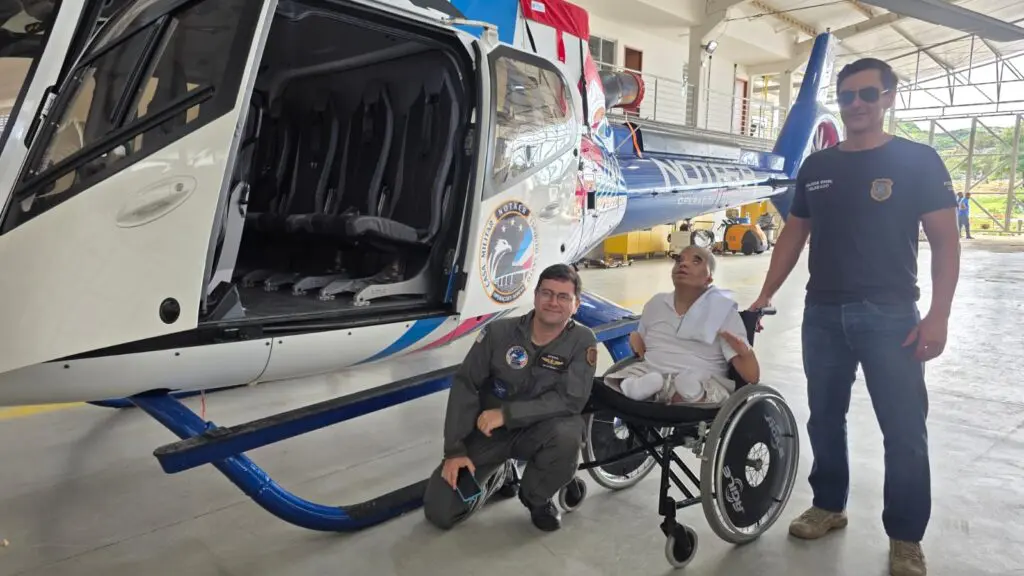 Foto de dois delegados ao lado de um jovem em uma cadeira de rodas, posando para uma foto ao lado de um helicóptero.