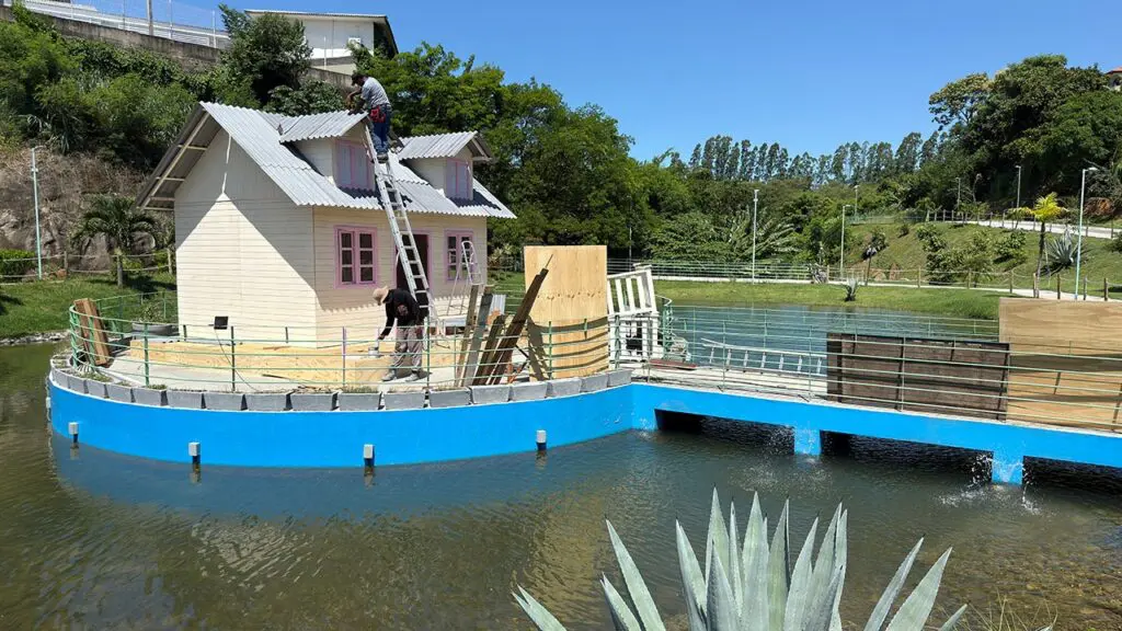 Imagem de um parque com uma casa decorativa no meio do lago, e dois homens fazendo manutenção no local.