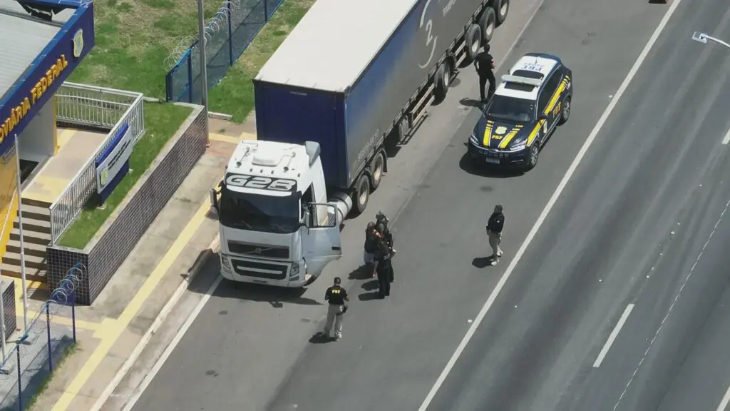 Imagem aérea de um posto da Polícia Rodoviária Federal, parando uma carreta, proximo a carreta há uma viatura da PRF e agentes prendendo um homem.