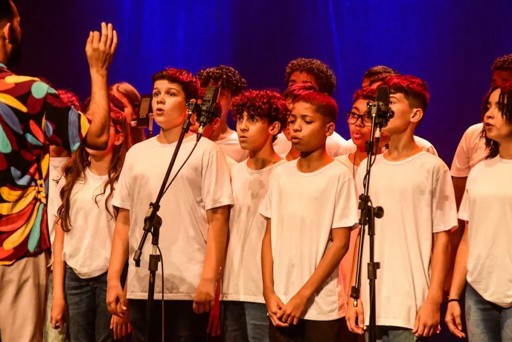 Imagem de um professor e, em sua frente, diversas crianças cantando.