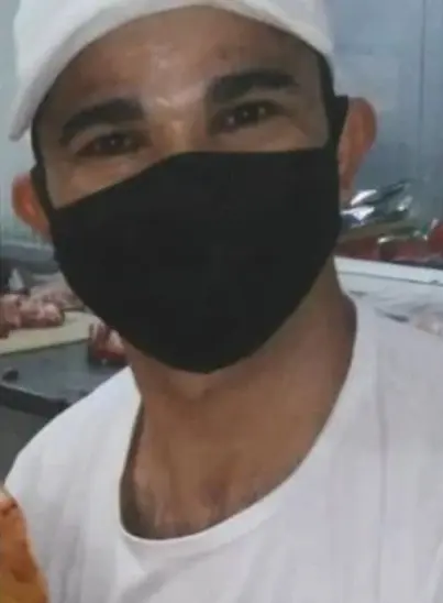 Imagem de um homem usando boné e máscara de pano, e no fundo uma mesa de um açougue.