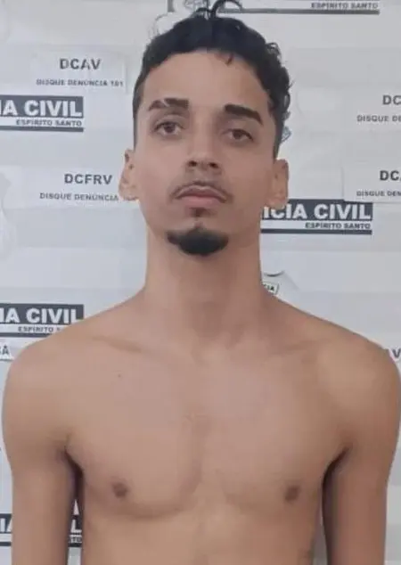 Imagem de um sujeito (Ruan Christyan Cardoso dos Santos, de 19 anos), preso pelo crime de latrocínio, em frente a uma parede de identificação da Polícia Civil.