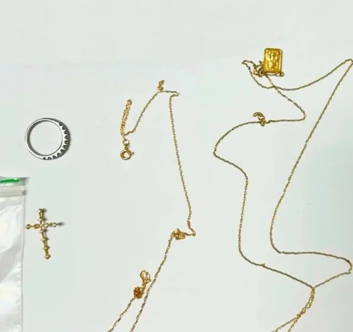 Sobre uma mesa, algumas joias: um anel e duas correntes de ouro.