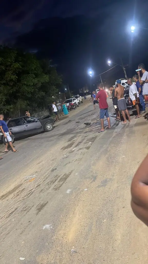 Imagem de uma avenida com dois carros batidos e diversas pessoas em volta.