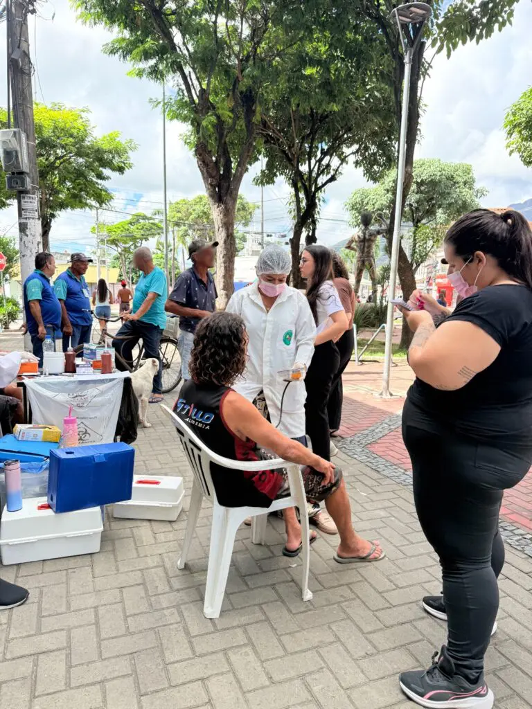 Imagem de uma praça, com uma equipe médica realizando exames em pessoas em condição de rua.