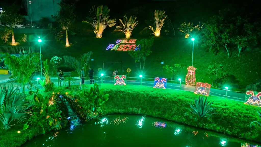 Imagem de uma praça próxima a uma lagoa, decorada com luzes, para comemorar a Páscoa.