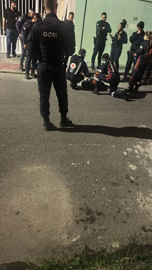 Socorristas do SAMU ao lado de um homem deitado no chão, baleado.