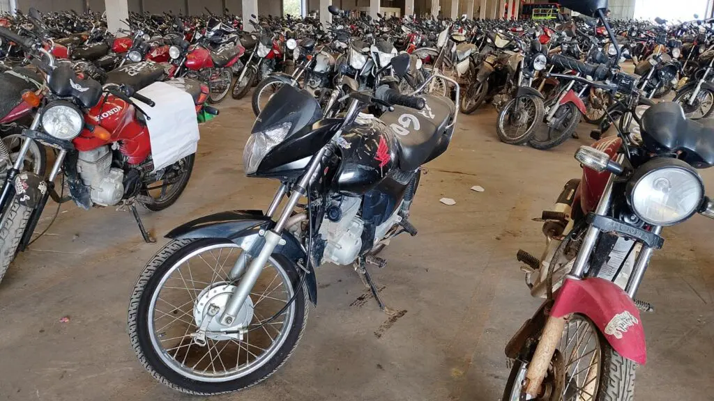 Imagem de uma motocicleta Honda/CG 150 Tutan EX, em um galpão, com diversas motos estacionadas ao fundo.