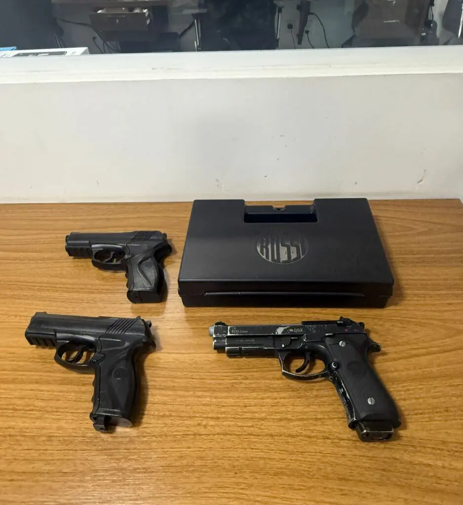 Sobre uma mesa uma maleta e três simulacros de pistolas. 