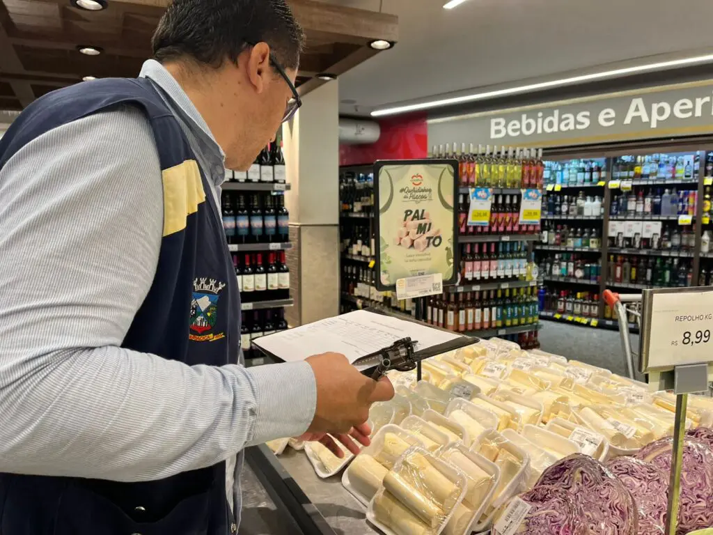 Um fiscal do Procon de Cariacica segurando uma prancheta em frente a uma mesa com exposição de palmitos e repolho roxo.
