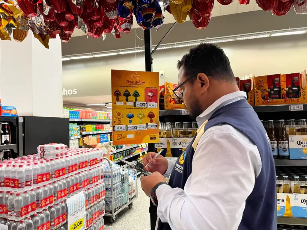 Um fiscal do Procon de Cariacica segurando uma prancheta em frente a uma parreira de ovos de Páscoa.