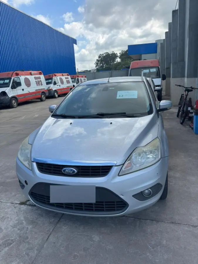 Um veículo (Ford Focus) estacionado em um pátio junto com outras ambulâncias danificadas.