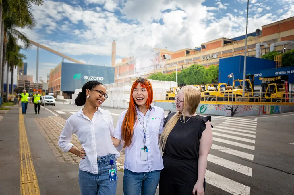 Imagem de três mulheres jovens abraçadas, tirando uma foto no pátio da empresa Suzano. 