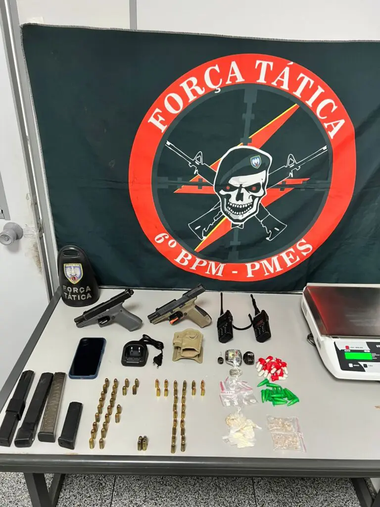 Sobre uma mesa, duas pistolas — uma calibre .380 e outra 9 mm —, três carregadores alongados, um carregador comum, dois rádios comunicadores e porções de drogas, como maconha, haxixe e pinos de cocaína.