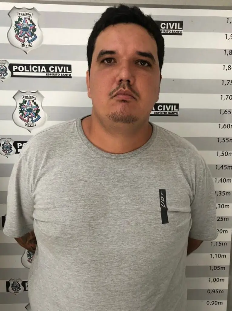Imagem de um homem (Jadson Correia Ferreira) em frente a uma parede com informações da Polícia Civil e marcações de altura.