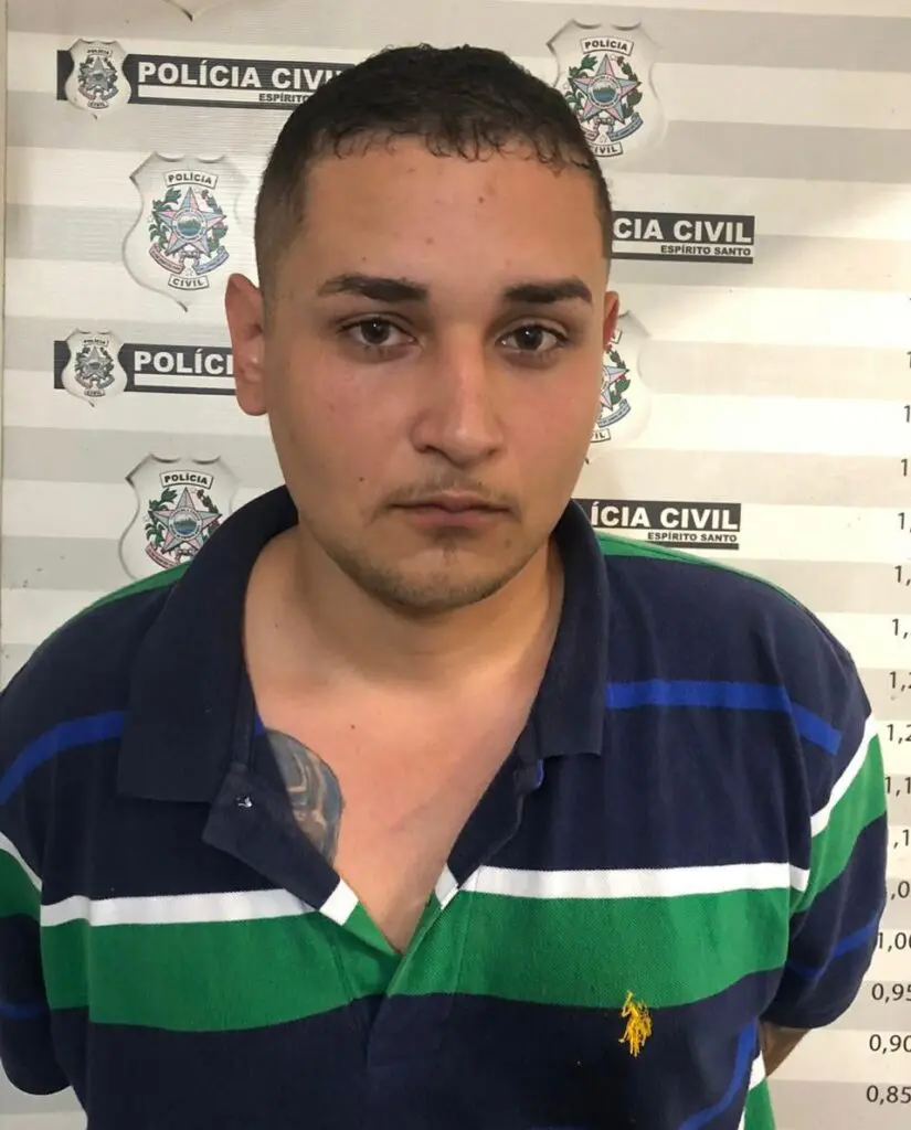 Imagem de um homem (Marcos Vinicius de Almeida Garcia Sepulcro) em frente a uma parede com informações da Polícia Civil e marcações de altura.