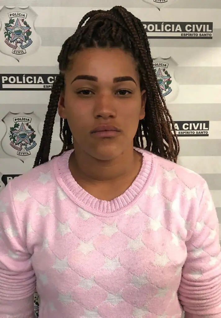 Imagem de uma mulher (Willyani Luciana Claudina Felicino) em frente a uma parede com informações da Polícia Civil e marcações de altura.