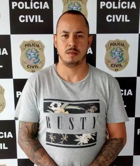 Imagem de um homem (Rodrigo Soares Ferreira) em frente a uma parede com informações da Polícia Civil e marcações de altura.