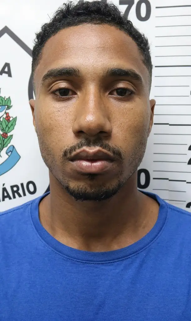 Imagem de um homem (Brendo Nascimento Correa) em frente a uma parede com informações da Polícia Civil e marcações de altura.