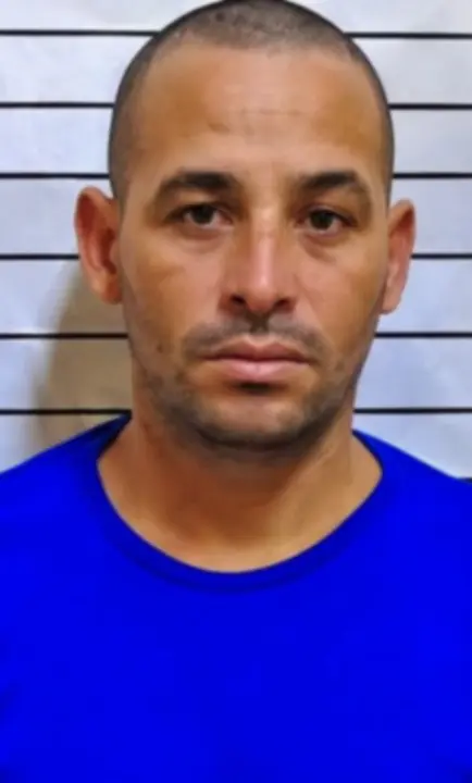 Imagem de um homem (Robson Gomes Realli) em frente a uma parede com informações da Polícia Civil e marcações de altura.