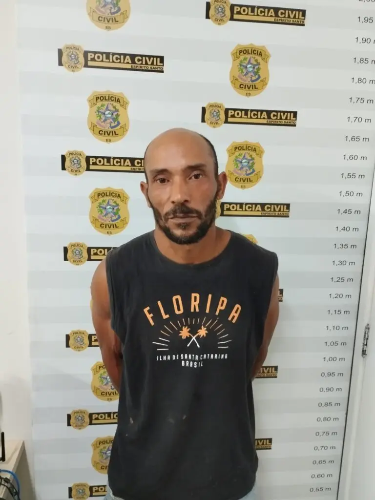 Um homem (Elias Grigorio de Laia, de 46 anos) em frente a uma parede com marcações de altura, como as que a Polícia Civil utiliza após a prisão de um suspeito.