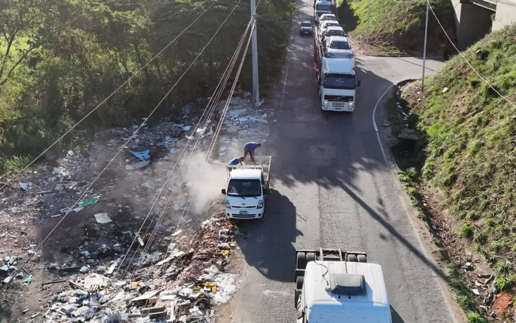 Imagem aérea de uma avenida com um caminhão estacionado em um dos lados, enquanto dois homens descartam lixo.