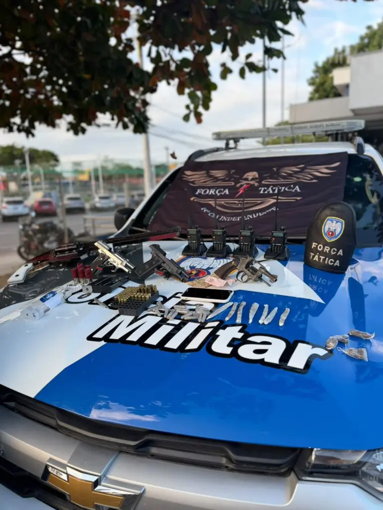 Sobre o capo de uma viatura da Polícia Militar duas pistolas, um revólver, uma espingarda calibre 12 de fabricação artesanal, munições, rádios comunicadores, drogas, dinheiro em espécie e uma granada.