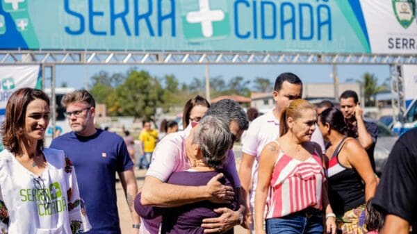 Prefeito Sérgio Vidigal abraçando uma senhora em frente a placa de divulgação do Serra mais Cidadã
