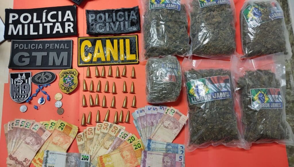 Dinheiro, sacos de maconha, pinos de cocaína sobre a uma mesa vermelha da Policia Militar