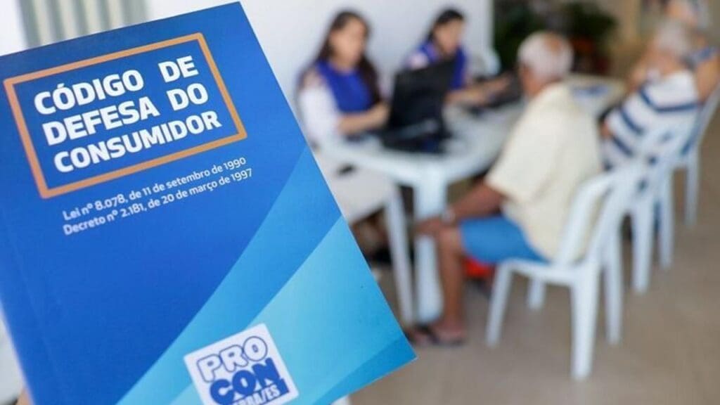 Código de defesa do consumidor em destaque na mão de um cliente e ao fundo desfocado atendentes do Procon atendendo clientes em uma mesa