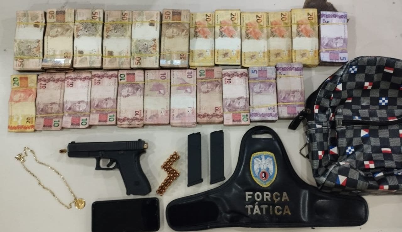 Sobre a mesa da Policia Militar oitenta mil e dez reais, uma pistola 9 milímetro, um celular, dois carregadores de pistola, uma mochila e uma braçadeira da policia militar