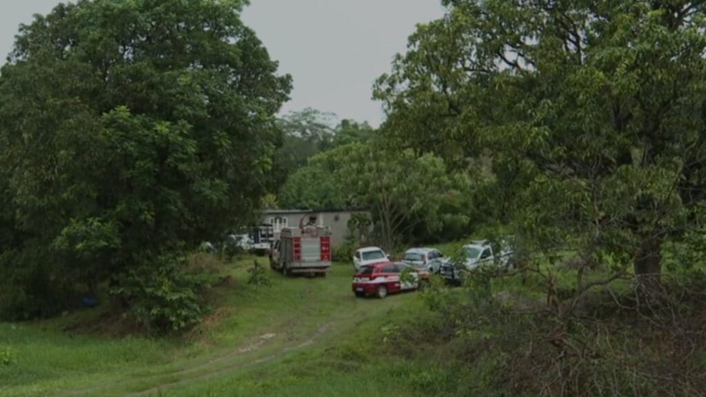 Viaturas do Bombeiro, IML atendendo ocorrência em Sitio, ao fundo casa com indícios de incêndio