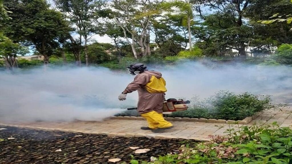 Agente da Vigilância Ambiental em Saúde (VAS) com roupas especial espalhando o fumace em rua