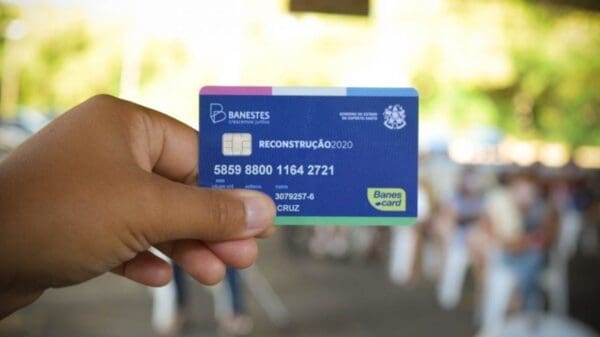 Foto com fundo desfocado e uma mão segurando um cartão azul chamado Cartão Cidadão para vítimas das fortes chuvas receberem benefícios do Governo