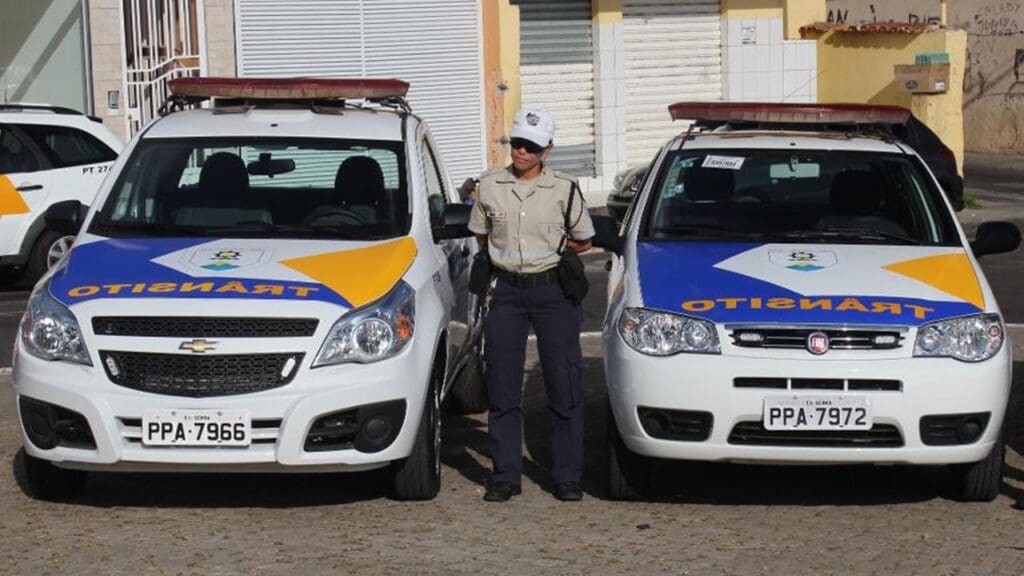 Duas viaturas estacionadas e uma agente de transito para ao centro