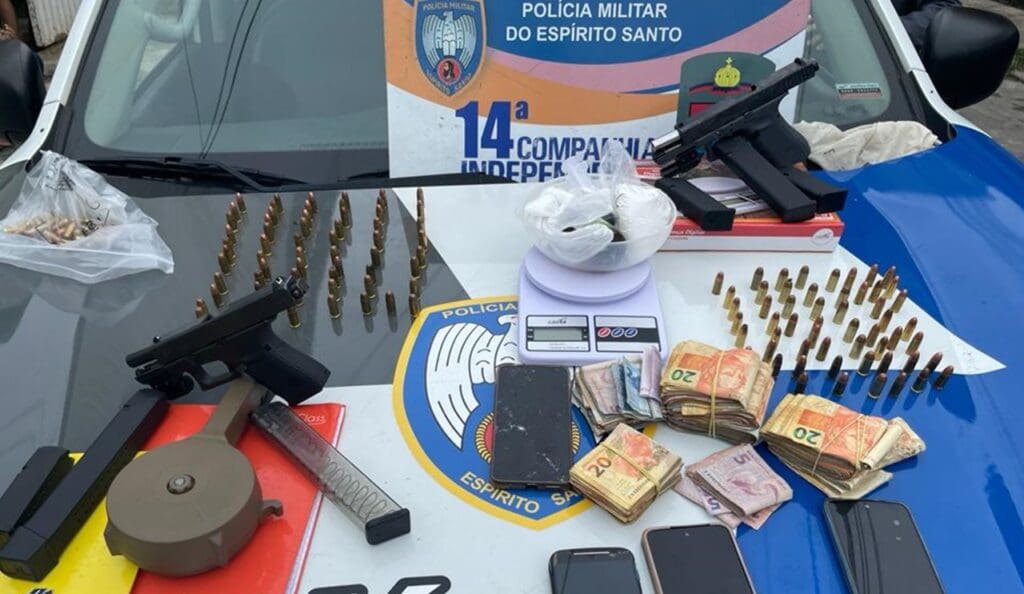 Sobre o capo da viatura da Polícia Militar duas pistolas, quatro celulares, grande quantidade de dinheiro fracionado, pentes carregadores e dezenas de munições